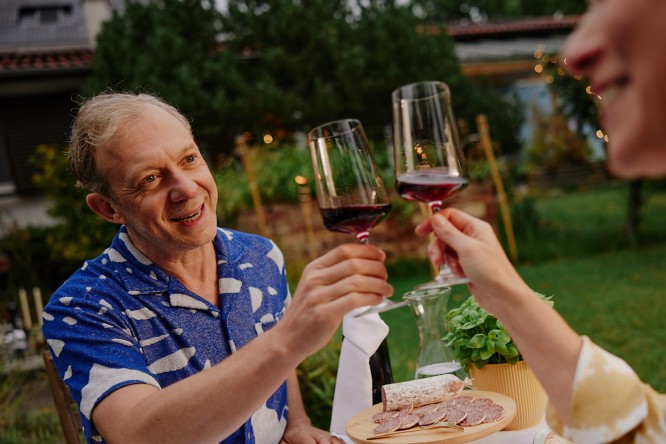 Älteres Paar sitzt beim Abendessen im Garten und stößt mit Wein an